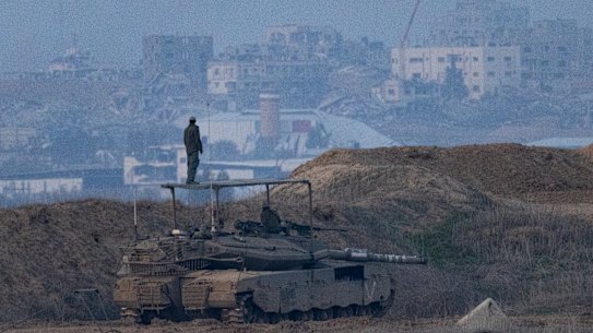 An Israeli soldier stands on a tank near the border with the Gaza Strip as seen from a position on the Israeli side of the border .