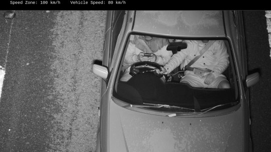 This driver was captured with both hands on a mobile phone while the passenger held the steering wheel.