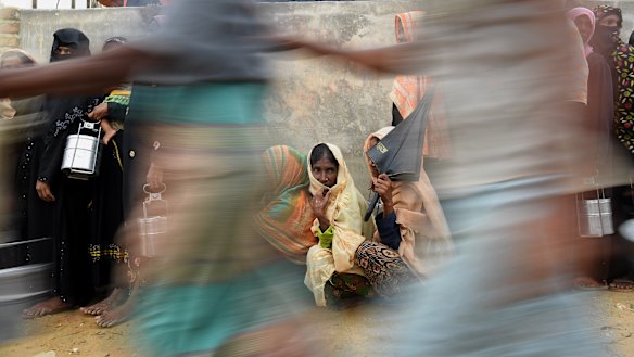 Rohingya refugee women wait in line as men run past for a meal provided by a Turkish aid agency.