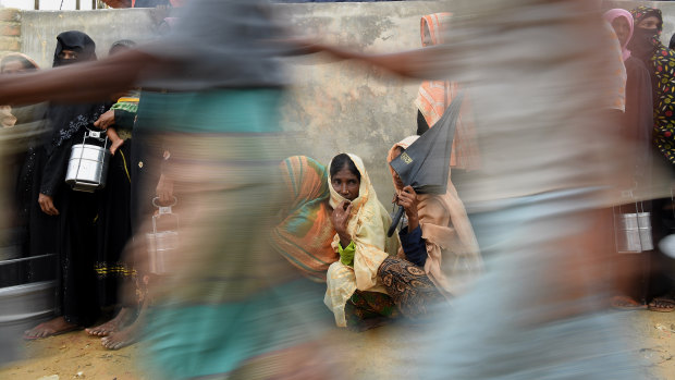 Rohingya refugee women wait in line as men run past for a meal provided by a Turkish aid agency.
