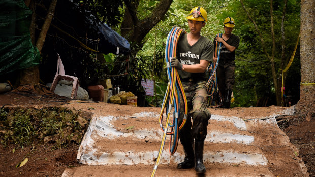 Thai volunteers bring back to the base camp the fibre optic cables that have failed to work inside the cave.