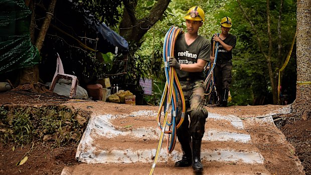 Thai volunteers bring back to the base camp the fibre optic cables that have failed to work inside the cave.