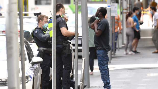 Police officers in the city stop a man and ask him to put on a mask.