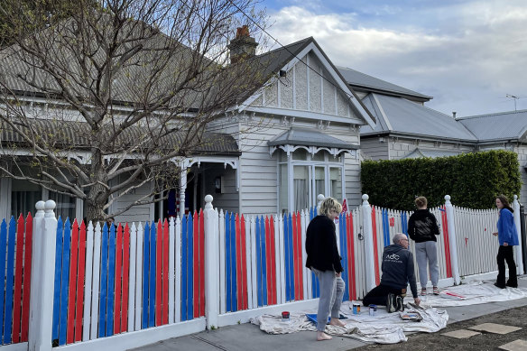 Members of the Willson/Sherman family paint the front fence of their Seddon home in the red, white and blue of the Western Bulldogs.