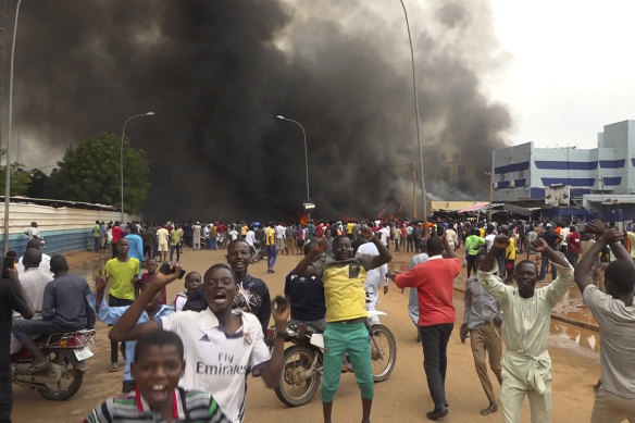 With the headquarters of the ruling party burning in the back, supporters of mutinous soldiers demonstrate in Niamey, Niger.