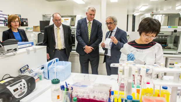 Minister for Medical and Health Research Meegan Fitzharris, with  provost of ANU Mike Calford, health director general Mike De 'Ath and ANU professor of medicine Mathew Cook at Canberra Clinical Genomics, while genomics technician Rong Liang works on far right. 