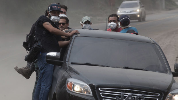 Rescuers and journalists evacuate the disaster zone as a column of smoke and ash rises from the Volcan de Fuego, on Tuesday.