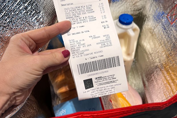 A Coles receipt being held up in front of a trolley containing a bag of groceries.