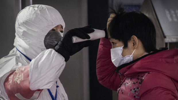A Chinese health worker checks the temperature of a woman entering a subway station in Beijing.