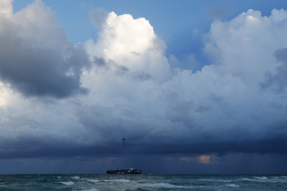 A container ship heads out to sea into bands of rain as a kitesurfer enjoys the winds off South Beach, Friday. All of Florida is under a state of emergency ahead of Hurricane Dorian. 