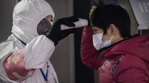 A Chinese health worker checks the temperature of a woman entering a subway station in Beijing.