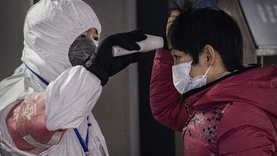 A Chinese health worker checks the temperature of a woman entering a subway station in Beijing.