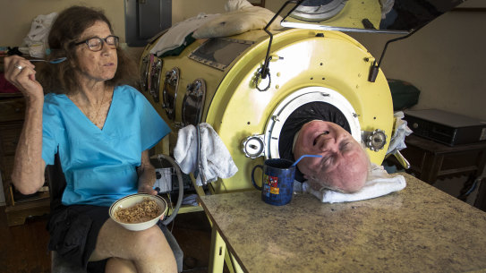Attorney Paul Alexander chats with caregiver and friend Kathryn Gaines as he drinks coffee and she eats breakfast beside his iron lung at his home in Dallas. 