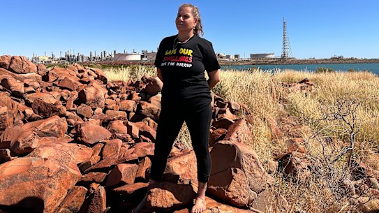Murujuga custodian Raelene Cooper standing on Murujuga, with Woodside’s Karratha plant in the background.
