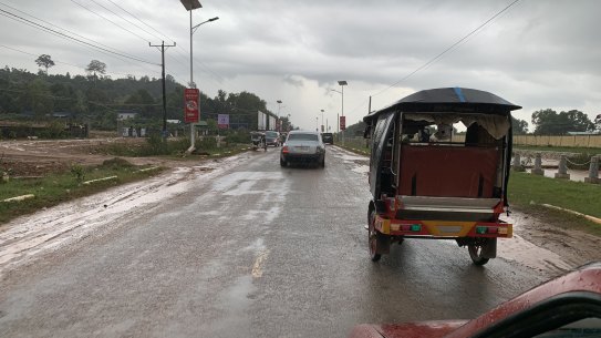 A Rolls-Royce and a tuk-tuk drive towards Sihanoukville Airport.
