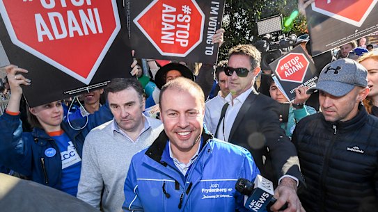 Treasurer Josh Frydenberg voting, surrounded by protesters carrying 'Stop Adani' placards.