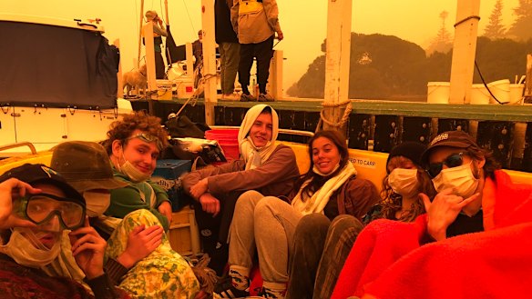 Mary O'Malley and others shelter on a borrowed boat at Mallacoota. The Royal Australian Navy will send ships as soon as possible to offer help to coastal towns hit by fire.
