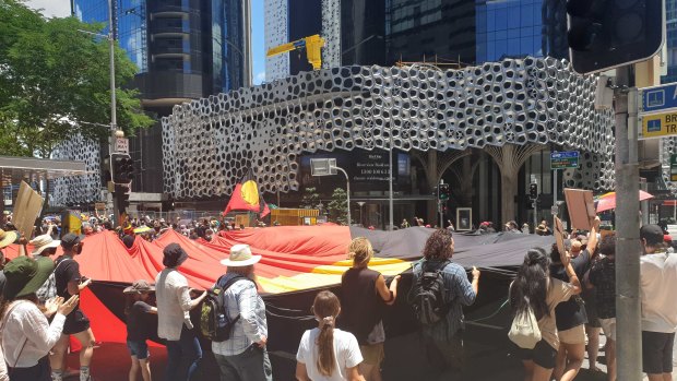 Invasion Day protesters carry a large Indigenous flag through Brisbane