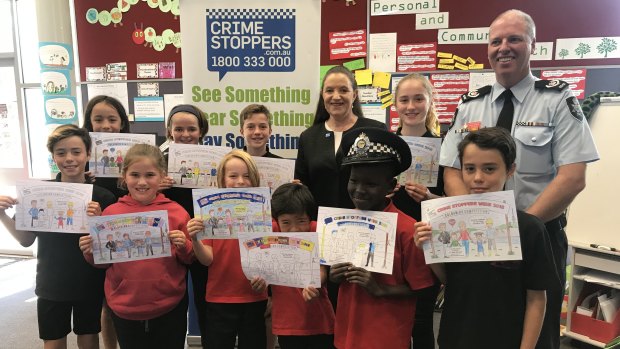 Crime Stoppers ACT region chair Diana Forester and ACT Policing Acting Superintendent Jason Kennedy with North Ainslie Primary School children, who are showing off their Crime Stoppers Week colouring in competition entries. 