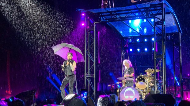 Singing in the rain: Adam Lambert, Brian May and Roger Taylor with various levels of shelter.