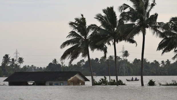 Two men row a boat through a flooded field in Alappuzha, Kerala, on Monday.