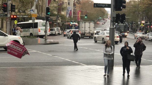 A poster is blown off a traffic light pole and pedestrians shield their faces as strong winds hit Sydney.
