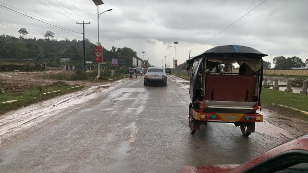 A Rolls-Royce and a tuk-tuk drive towards Sihanoukville Airport.