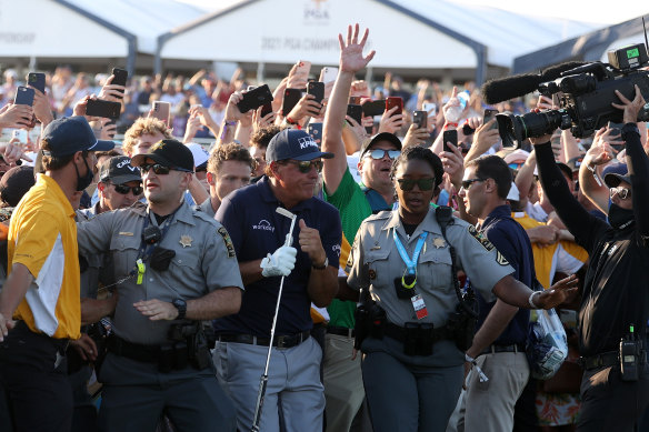 Phil Mickelson is assisted by security as he is followed up the 18th fairway by a gallery of fans after hitting his approach shot during the final round.