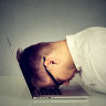 Stressed young man resting head on laptop.