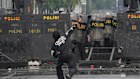 Police officers cover themselves with riot shields as a protester throws rocks, outside the parliament in Jakarta on Sunday.