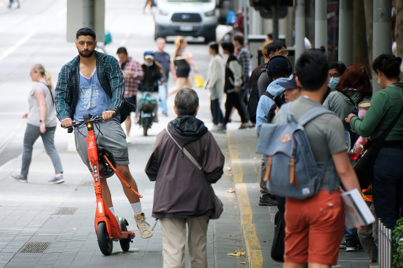 A man riding a hire scooter without a helmet in the CBD.
