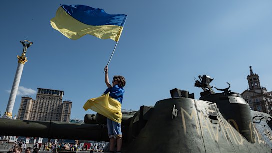 A boy holds a Ukrainian national flag on a captured Russian tank in central Kyiv.