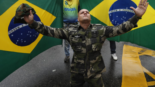 A Bolsonaro supporter dressed in fatigues, kneels in front of national flags in Rio de Janeiro, during a protest against his defeat in the presidential election.