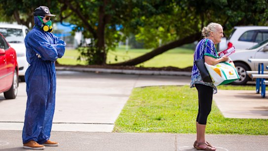 A voter wearing a protective suit and a gas mask stands spaced apart behind another voter outside a polling station during the local government elections in Noosa.