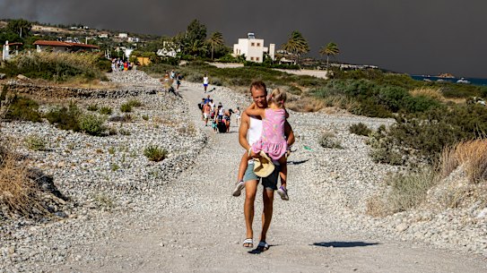 A man carries a child as they leave an area where a forest fire burns, on the island of Rhodes, Greece.
