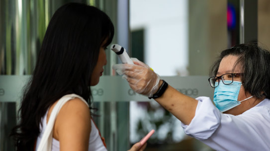 A security guard wearing a protective mask checks the temperature of a person entering an office building.