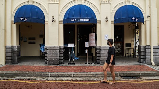 A pedestrian walks past signs for safety measures and promoting takeaway outside the entrance to a restaurant in the central business district of Singapore, on Wednesday, May 19, 2021. 