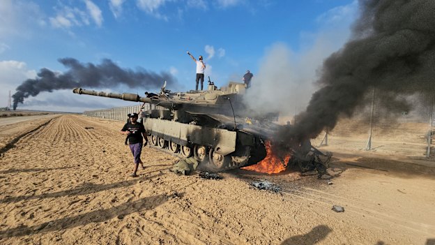 Palestinians celebrate by a destroyed Israeli tank at the Gaza Strip fence east of Khan Younis on October 7. 