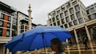 Women holding blue umbrella walking past the London Stock Exchange in London. 