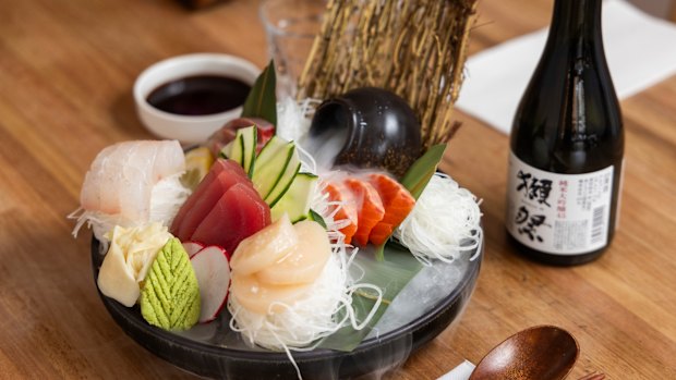 Tuna, kingfish, and salmon sashimi arrive wreathed in dry-ice fog against a sculpted backdrop of cucumber and radish.