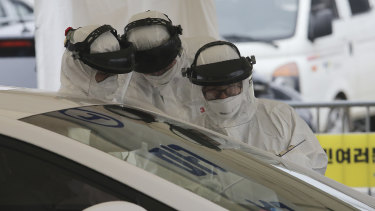 Medical staff wearing protective suits take samples from a driver with symptoms of the coronavirus at a "drive-through" virus test facility in Goyang, South Korea.