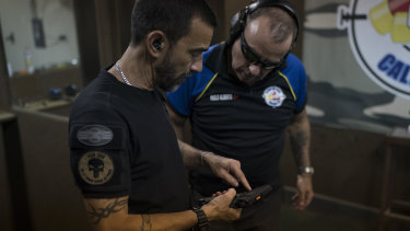 Rildo Anjos, owner of the Calibre 12 gun club, shows a pistol to club member Paulo Alberto as they stand at the shooting range in Sao Goncalo.