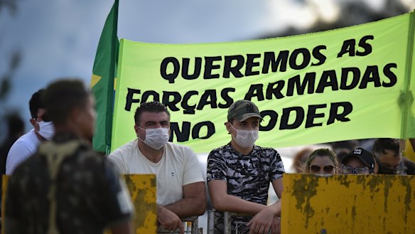 Supporters of Brazilian President Jair Bolsonaro stand with a banner that reads in Portuguese, “We want the armed forces in power,” outside his residence last year.