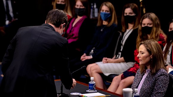 Supreme Court nominee Amy Coney Barrett watches as an aide tests her microphone during a confirmation hearing before the Senate Judiciary Committee.