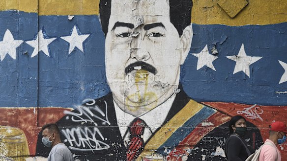 Pedestrians wearing protective masks walk by a mural of President Nicolas Maduro in Caracas, Venezuela, on Tuesday.
