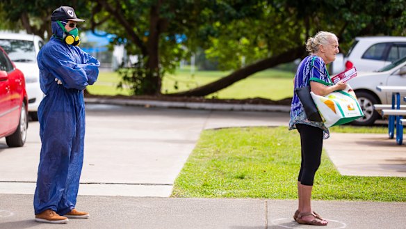 A voter wearing a protective suit and a gas mask stands spaced apart behind another voter outside a polling station during the local government elections in Noosa.
