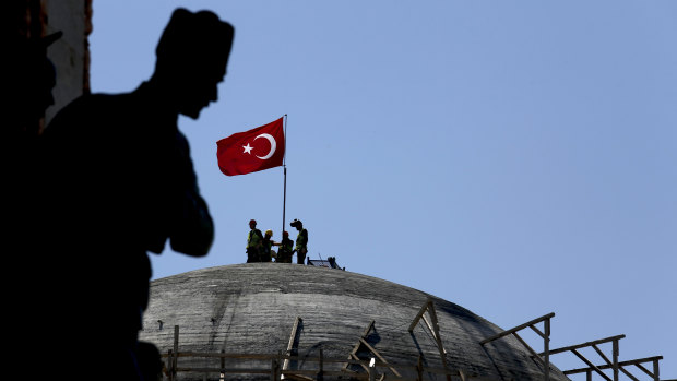 A sculpture of Turkey's founder Kemal Attaturk sits on the monument of the Republic as construction workers beyond place a Turkish national flag on the dome of the under-construction mosque in Taksim square in Istanbul.