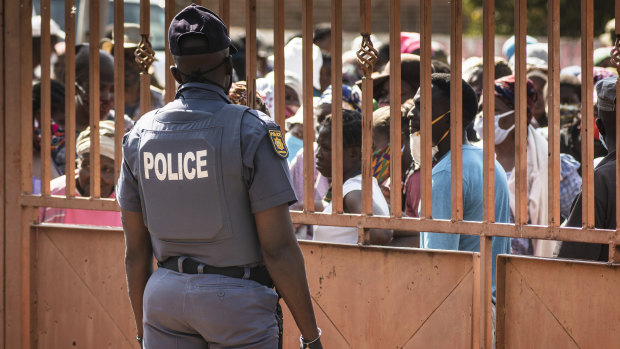 A police officer stands guard as residents queue to receive parcels of food aid in Finetown, south of Johannesburg.