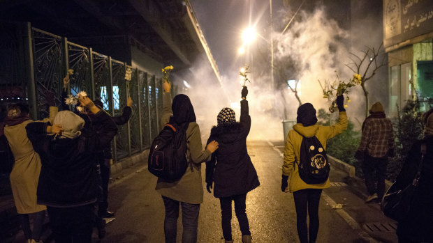 Protesters hold flowers as tear gas fired by police rises at a demonstration in front of Amir Kabir University in Tehran, Iran.