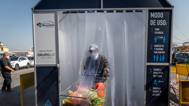 A person wearing a protective mask pushes a grocery cart through a decontamination chamber at the La Vega Central fruit and vegetable market in Santiago, Chile.